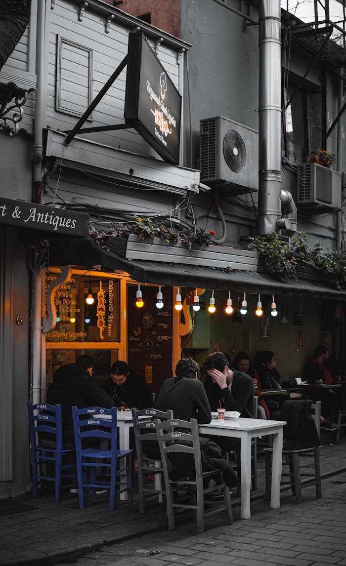 Charming street café with patrons enjoying evening ambiance under hanging lights.